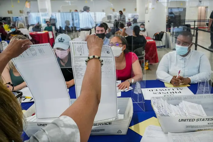 A New York City Board of Election staff member, left, shows a ballot to a campaign observer as primary election absentee ballots are counted during the 2021 election cycle. Republican and Conservative Party leaders are suing the state over the way it currently processes absentee ballots.